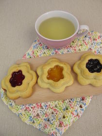 Mit Marmelade gefüllte Blümchenkekse und Tee auf einem Häkeldeckchen von Heike Rau