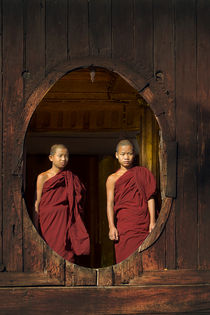 Two young buddhist monks at a wooden window in Myanmar by nilaya
