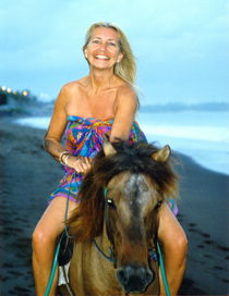 Beautiful woman riding a horse on a black sand beach at sunset by nilaya