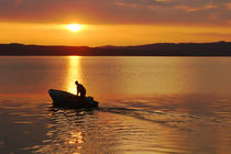 fisherman with motorboat at the lake in sunrise von Christian Zirsky