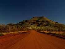 Australia dirt road with red sand in front of green hill by Bastian Linder