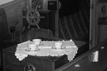 Flower patterned tea cups are laid out on a doily near the helm of a vintage wooden boat - monochrome by Intensivelight Panorama-Edition