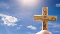 Hand hält Kreuz in den Himmel