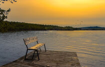 dreamy Swedish lake in the sunset with a bench to rest in the foreground von Margit Kluthke
