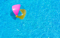 Inflatable colorful beach ball float on rippled blue swimming pool von Alex Winter