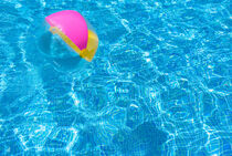 Floating inflatabel beach ball on swimming pool water surface by Alex Winter