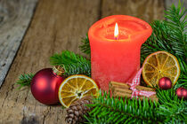 Red burning candle flame with fir tree branches wreath and ornaments decoration on wooden table by Alex Winter