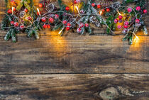 Christmas background with fir branches, pine cones, red berries and lights on wood by Alex Winter
