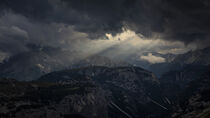 Sunbeams through dark clouds in the sky above Dolomite Alps mountains by Bastian Linder