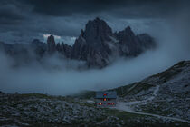 Rifugio Lavaredo mountain cabin with hiking trail in front of Dolomite Alps mountains with fog at Three Peaks in Italy from above during night by Bastian Linder