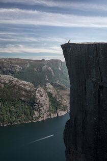 Woman sitting on the ridge of Preikestolen rock with view into Lysefjord in Norway by Bastian Linder
