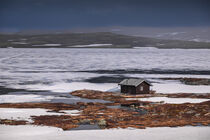 Hut at the waterfront of a frozen lake in the landscape of Hardangervidda National Park in Norway by Bastian Linder