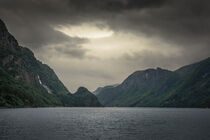 Norwegian fjord with waterfall and dark moody clouds in the sky by Bastian Linder