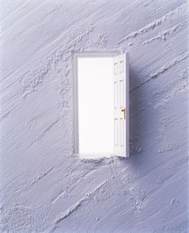 Open white door floating in center of light grey plaster wall by Panoramic Images