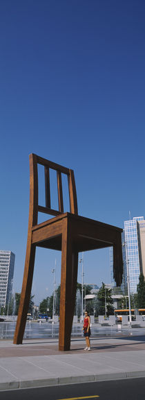 Woman standing under a sculpture of large broken chair, Geneva, Switzerland by Panoramic Images