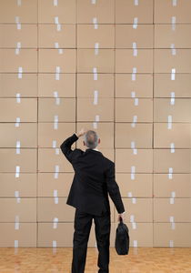 Businessman facing a cardboard boxes wall by Sami Sarkis Photography