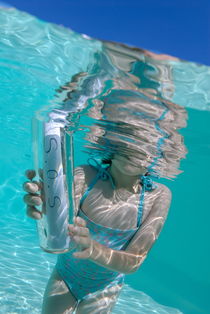Girl (6-7) in pool holding bottle with SOS message by Sami Sarkis Photography