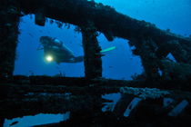 Woman diver with torch exploring shipwreck by Sami Sarkis Photography