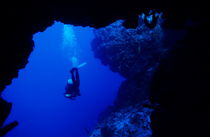 Diver swimming out of a cave. by Sami Sarkis Photography
