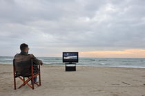 Man watching TV on beach at sunset by Sami Sarkis Photography