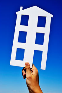 Hand holding house shape on blue sky by Sami Sarkis Photography