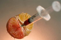 Syringe needle jabbed into a mandarin showing the possibility of genetically modified food. by Sami Sarkis Photography