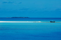 Fishing boat anchored on a white sand beach with a tropical island in the background by Sami Sarkis Photography