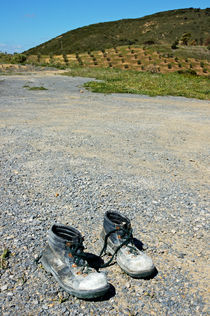 Old pair of worn out boots sitting on stony asphalt. von Sami Sarkis Photography