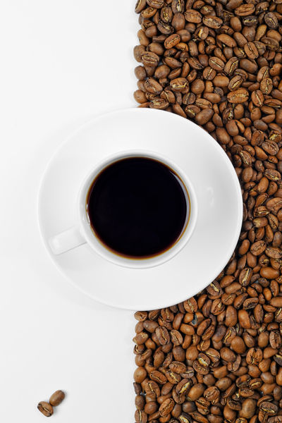 Coffee-in-white-cup-on-saucer-placed-on-background-of-coffee-beans-and-white
